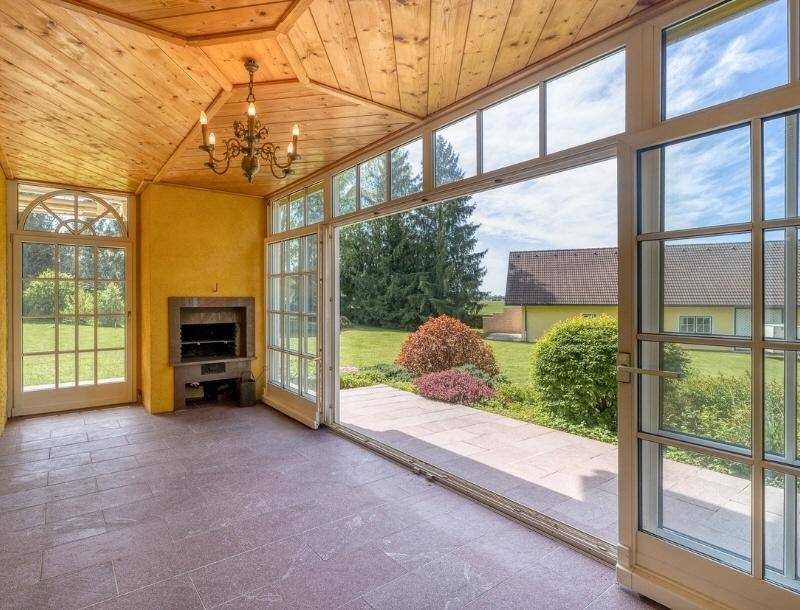Heller Wintergarten mit großen Glasfronten, integriertem Grillkamin und Zugang zum Garten.