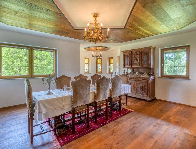Eleganter Essbereich mit langem Holztisch, Holzkassettendecke und großen Fenstern mit Blick ins Grüne.