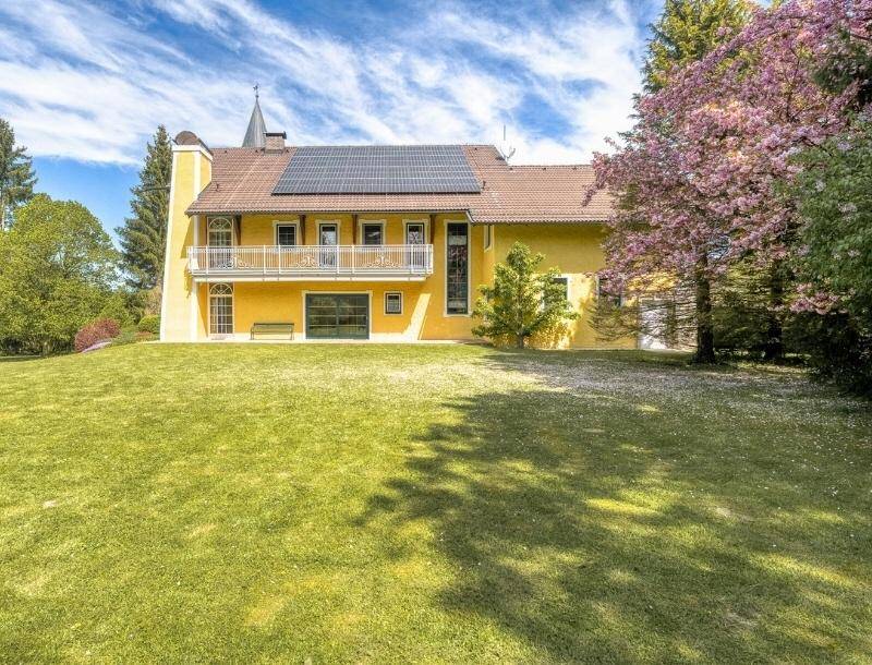 Rückansicht des Hauses mit Balkon, Solaranlage auf dem Dach und weitläufiger Rasenfläche.