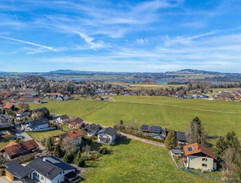 Weitläufige Luftaufnahme einer ländlichen Siedlung mit Feldern, einem großen See und Bergen im Hintergrund.