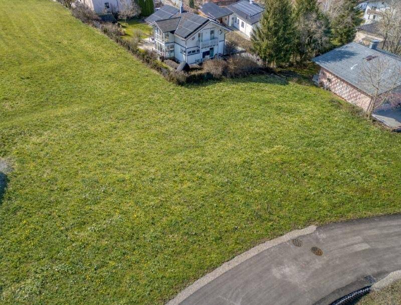 Großes grünes Grundstück mit angrenzender Straße und einem modernen Haus mit Solaranlage im Hintergrund.