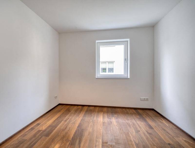 Kleiner, heller Raum mit Holzboden und einem Fenster, geeignet als Kinder- oder Arbeitszimmer.