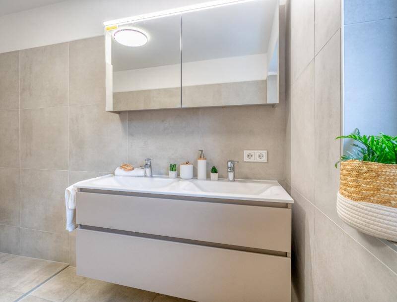 Modernes Badezimmer mit schwebendem Waschtisch, Spiegelschrank und großen Fliesen.