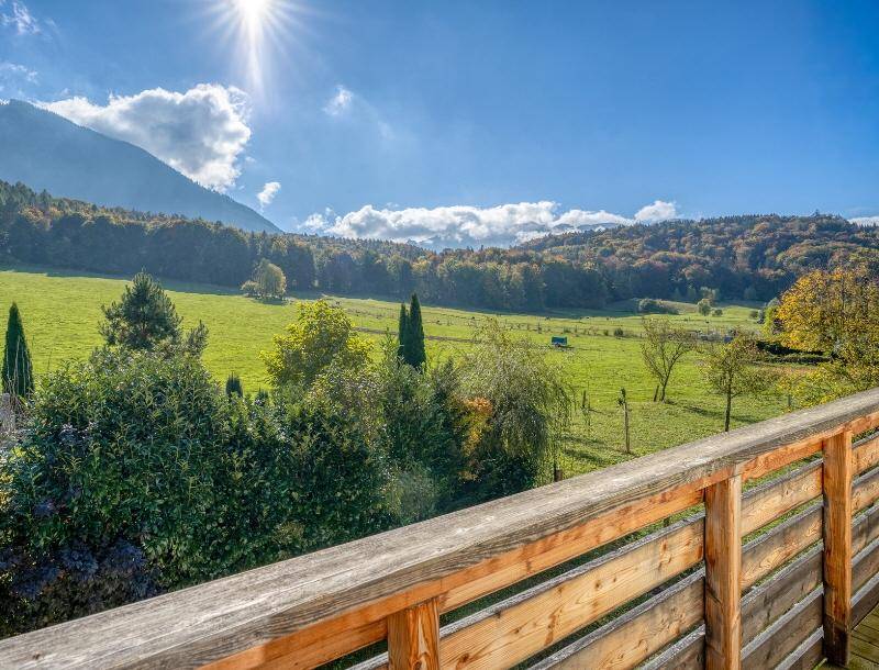 Weitläufiger Blick über grüne Wiesen und bewaldete Berge unter strahlend blauem Himmel.