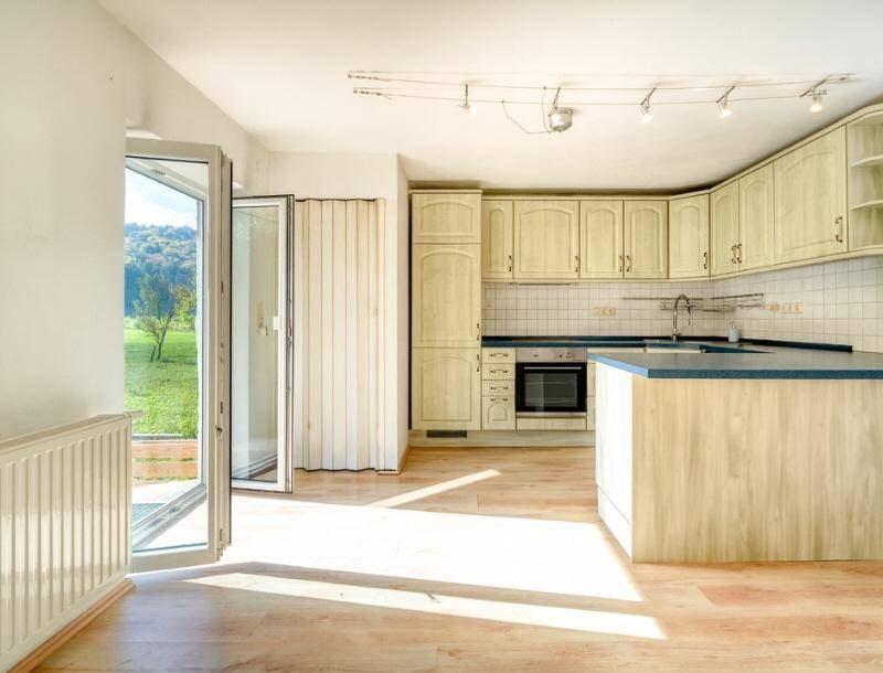 Helle Küche mit hellen Holzschränken und Zugang zum Garten, durchflutet von Sonnenlicht.