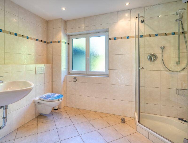 Gefliestes Badezimmer mit Dusche, WC und Waschbecken, ausgestattet mit einem Fenster für Tageslicht.