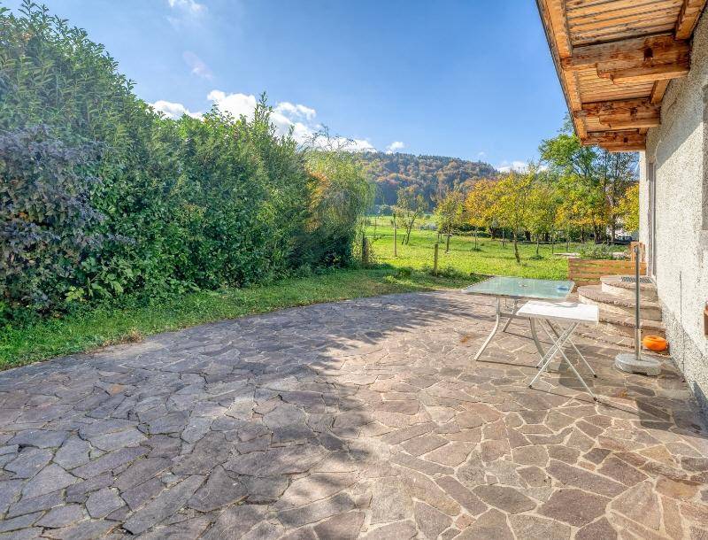 Gepflasterte Terrasse mit kleinem Tisch, umgeben von Hecken und Blick ins Grüne.