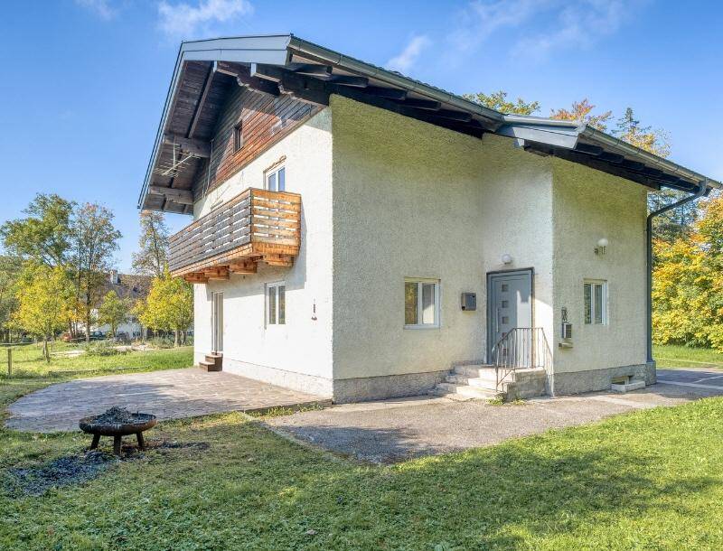 Seitenansicht des Hauses mit Eingangsbereich, Balkon und einer Feuerstelle im Garten.
