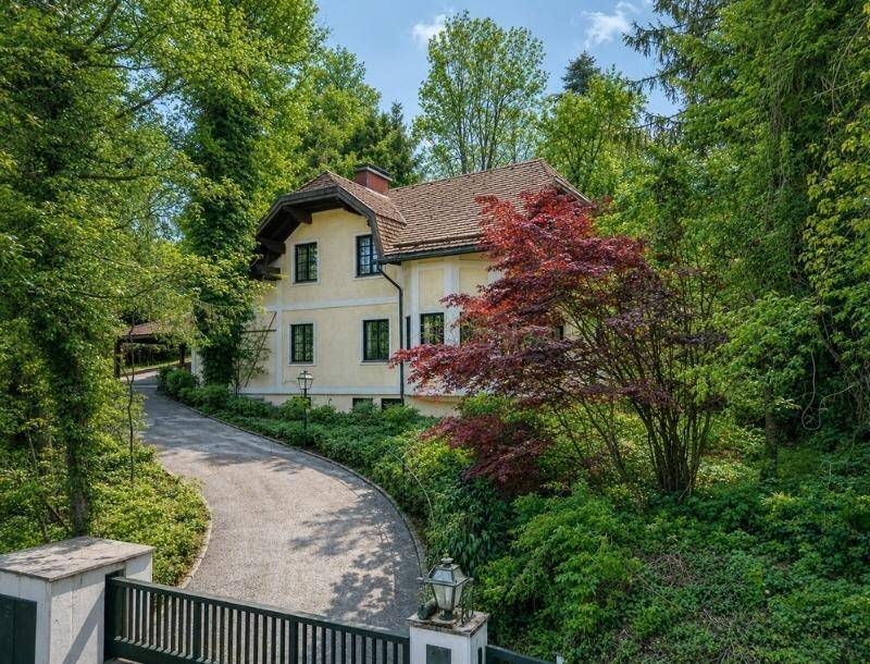 Zufahrt zum Anwesen mit schmiedeeisernem Tor, umgeben von üppiger Vegetation und Bäumen.