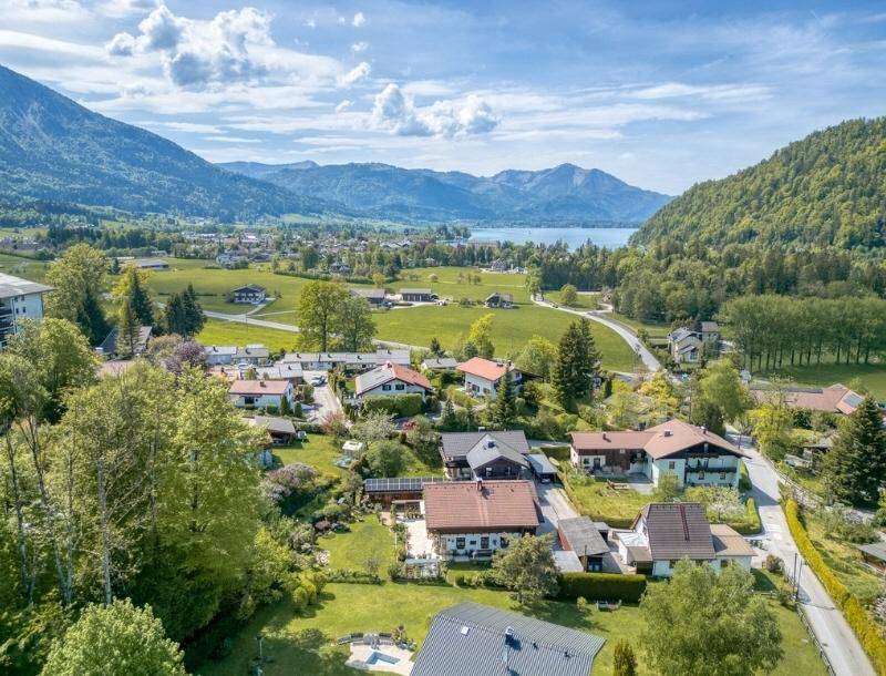 Malerische Luftaufnahme der Wohngegend mit See und Bergen im Hintergrund unter blauem Himmel.