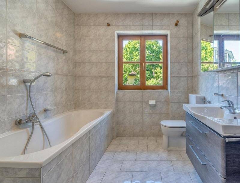 Gefliestes Badezimmer mit Badewanne, Fenster und Doppelwaschbecken.