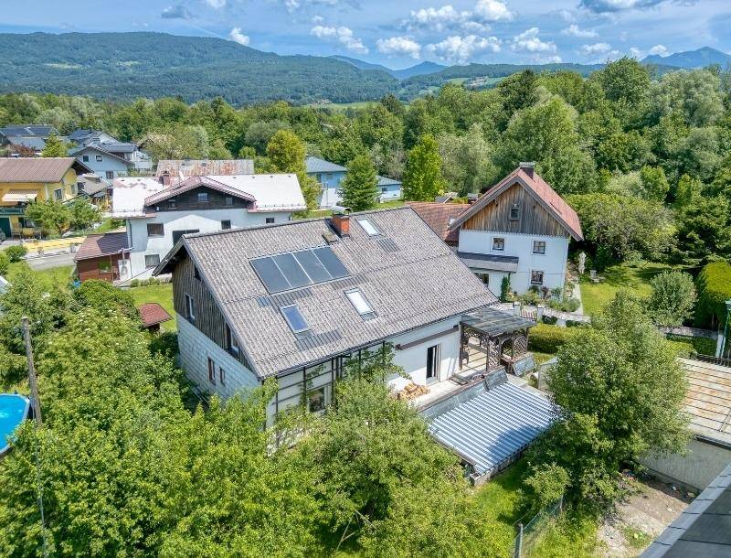 Luftaufnahme eines Hauses mit Photovoltaikanlage auf dem Dach und umliegender Natur.
