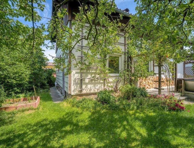 Seitlicher Gartenbereich mit Holzstapel und einem kleinen Hochbeet.