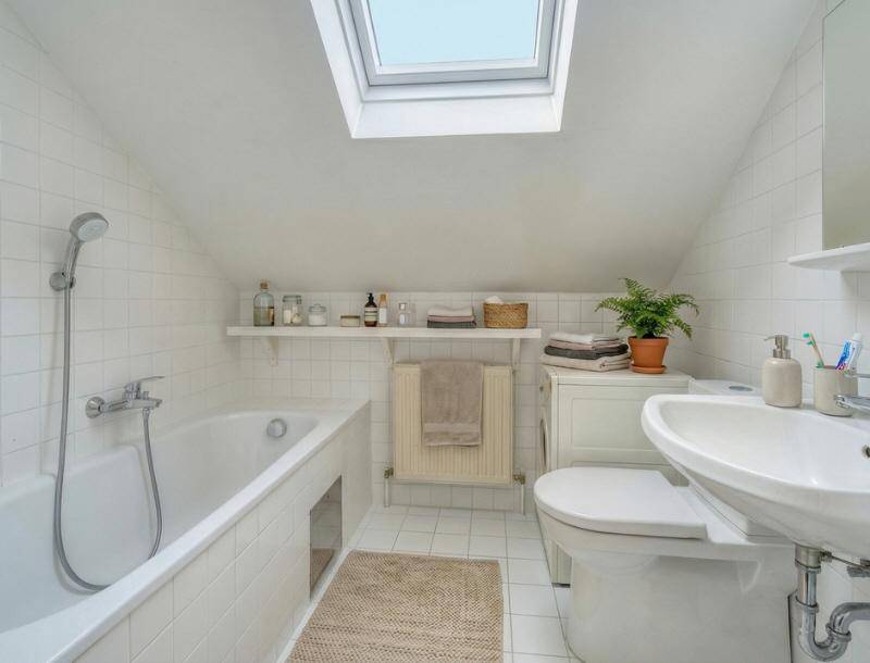 Helles Badezimmer mit Badewanne, WC, Waschbecken und Dachfenster.