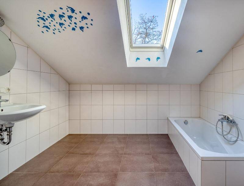 Badezimmer im Dachgeschoss mit Badewanne, Waschbecken und einem großen Dachfenster für Tageslicht.