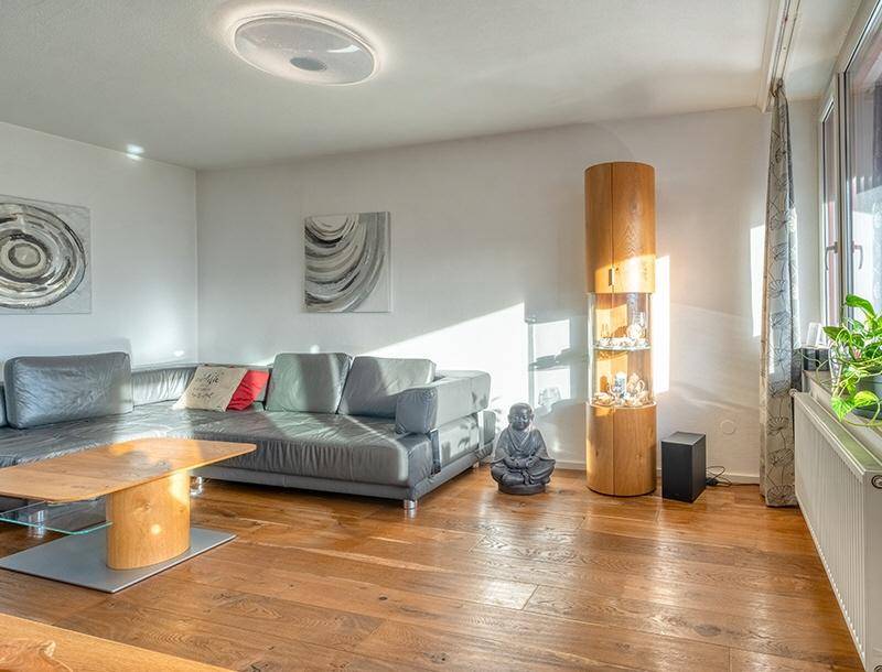 Helles Wohnzimmer mit Holzboden, bequemer Couch und dekorativen Elementen in modernem Stil.
