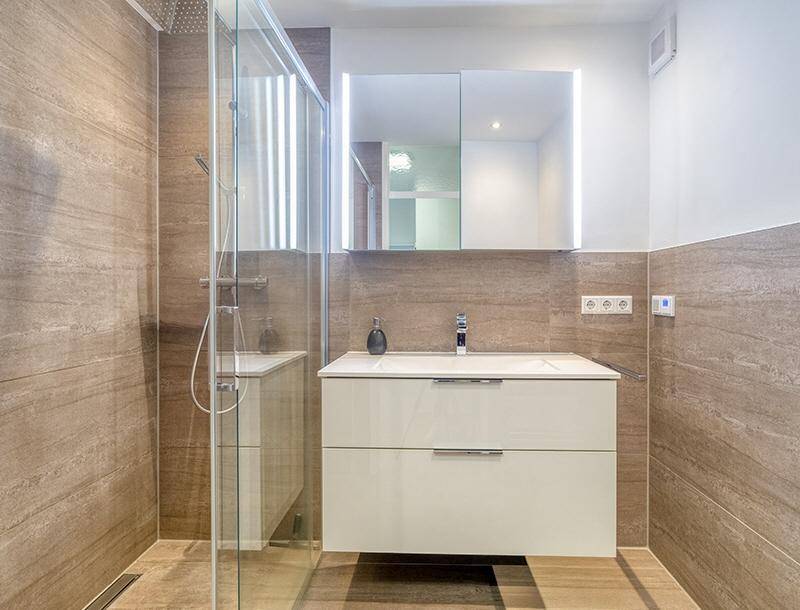 Modernes Badezimmer mit begehbarer Dusche, schwebendem Waschtisch und beleuchtetem Spiegelschrank.