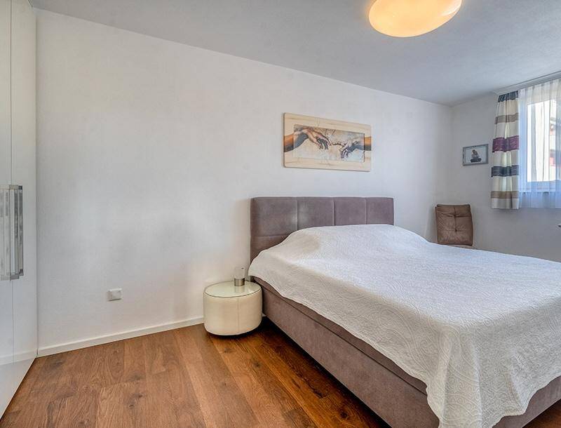 Helles Schlafzimmer mit Holzboden, großem Bett und einem Fenster, das Tageslicht hereinlässt.