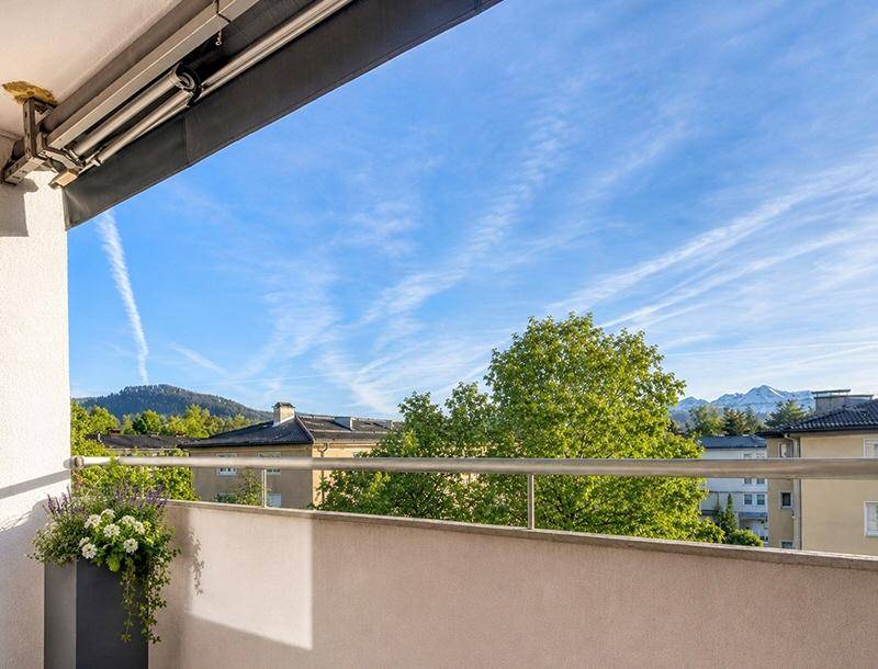 Balkon mit grüner Aussicht auf Bäume und Berge unter einem strahlend blauen Himmel.