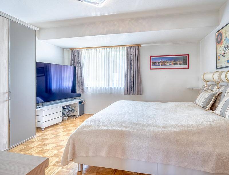 Schlafzimmer mit großem Bett, Kleiderschrank und Fernseher, ausgestattet mit Parkettboden.