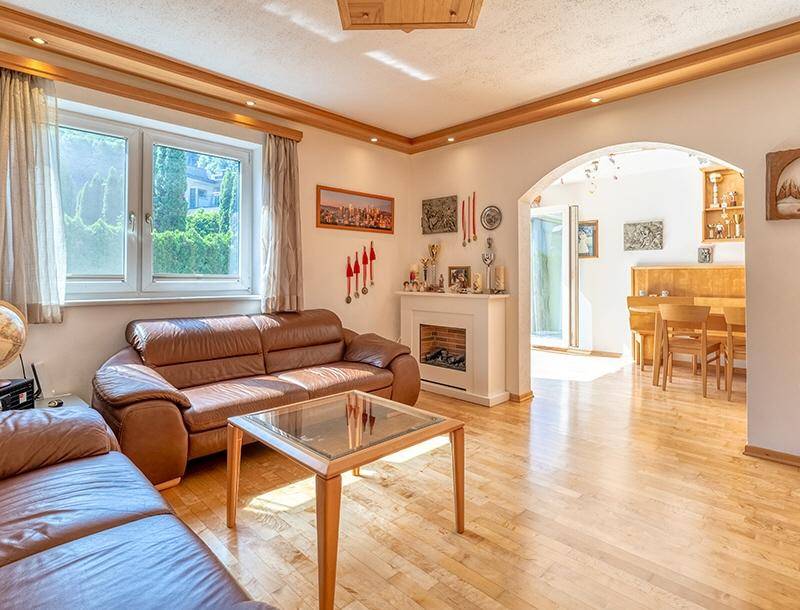 Helles Wohnzimmer mit braunen Ledersofas, Kamin und Holzboden, offen zum Essbereich.