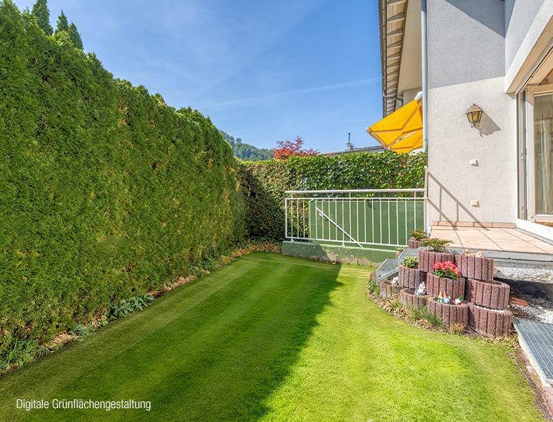 Gepflegte Rasenfläche neben einer hohen Hecke mit kleiner Terrasse und gelber Markise unter blauem Himmel.