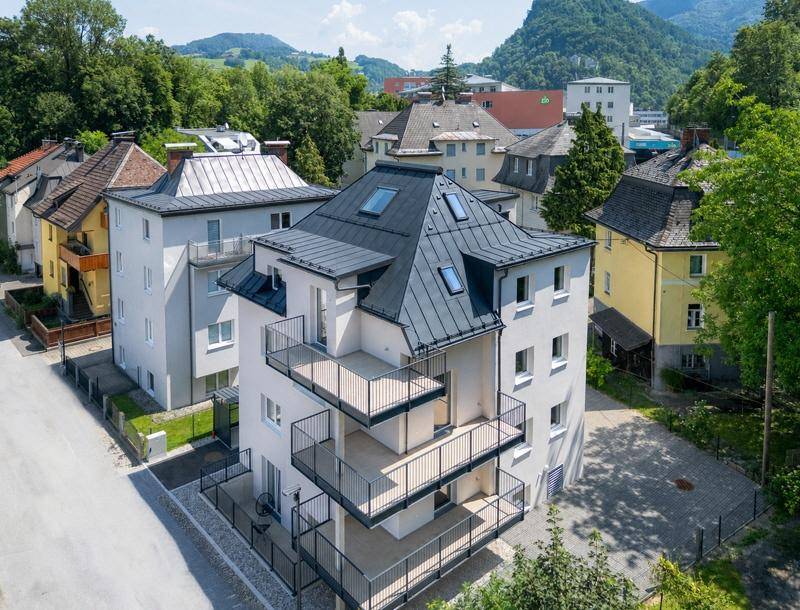 Modernes Neubaugebäude mit mehreren Balkonen und Blick auf die umliegende grüne Landschaft und Berge.