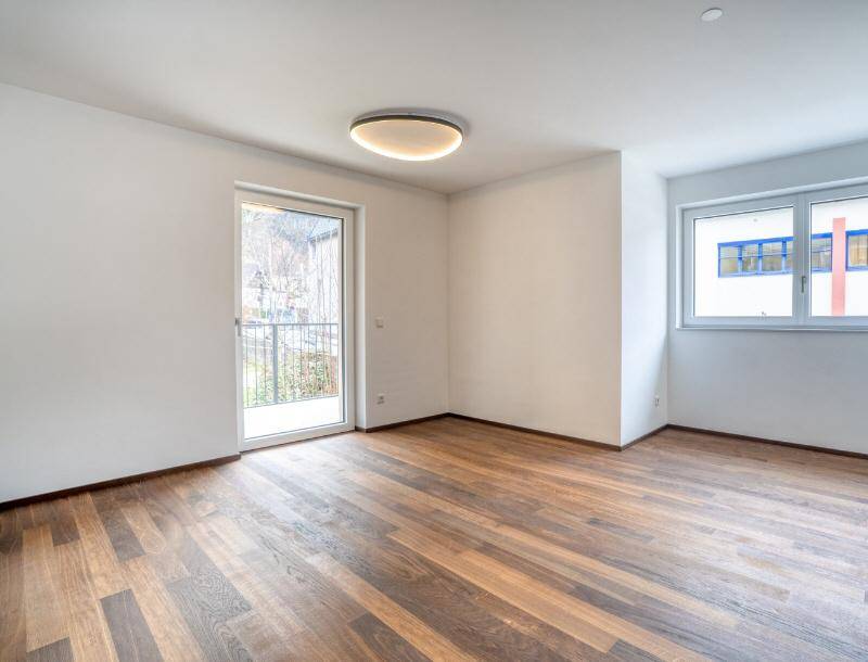 Heller, unmöblierter Raum mit hochwertigem Holzboden, großen Fenstern und direktem Zugang zu einem französischen Balkon.