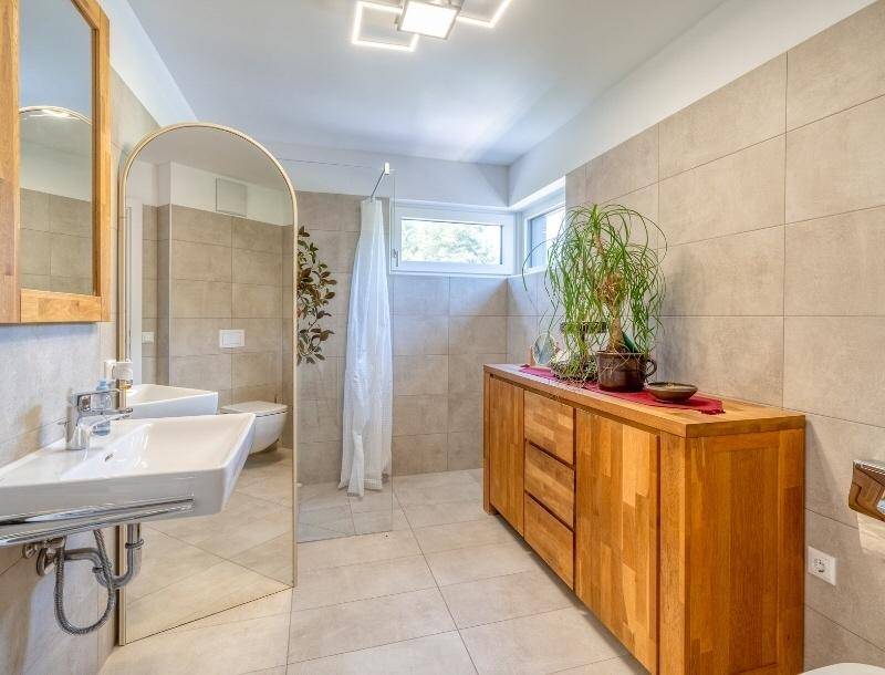 Modernes Badezimmer mit Fliesen, Holzunterschrank, Waschbecken und Duschbereich.