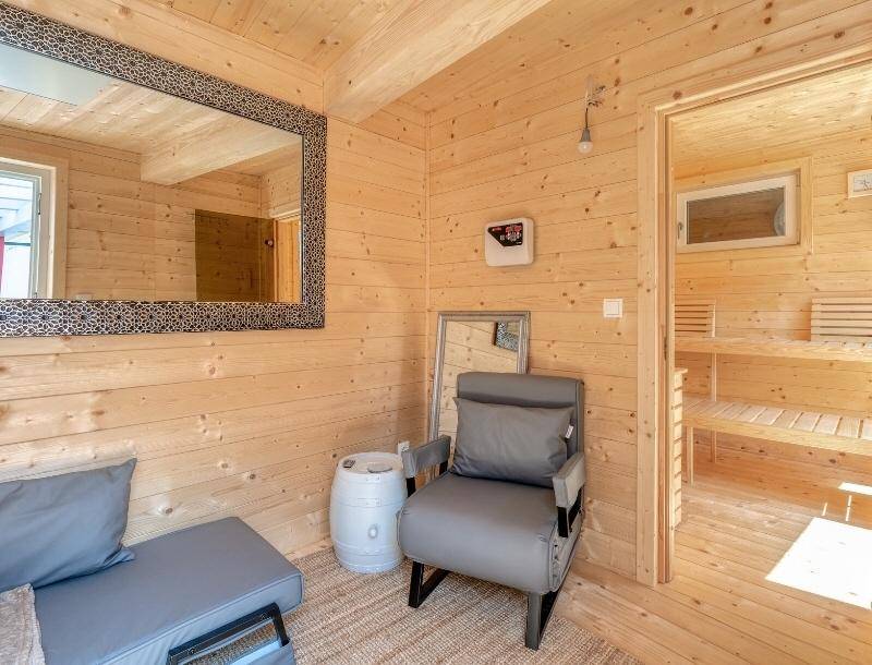 Gemütlicher Wellnessbereich mit Holzverkleidung, Sitzgelegenheiten und Zugang zur Sauna.