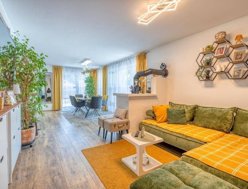 Gemütlicher Wohn-Essbereich mit grünem Sofa, Holzboden und farbenfroher Dekoration.