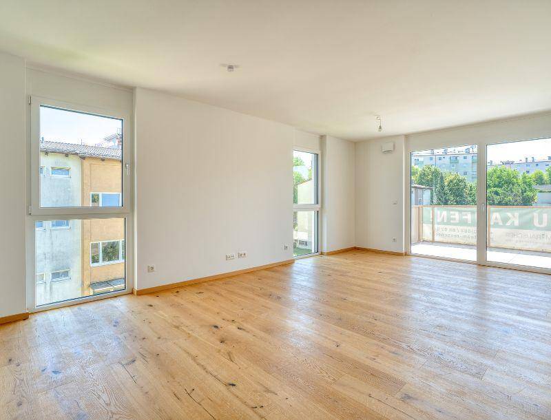 Großzügiger, lichtdurchfluteter Raum mit Holzboden und Zugang zu einem Balkon, ideal für Wohnzwecke.