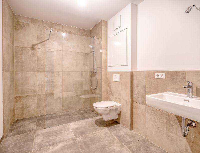 Modernes Badezimmer mit begehbarer Dusche, Wand-WC und beigefarbenen Fliesen.