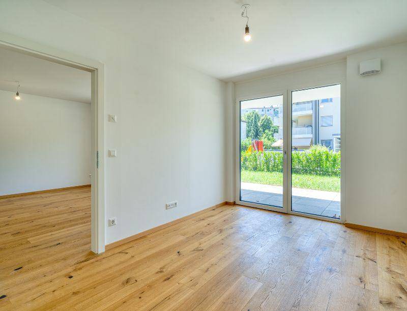 Lichtdurchflutetes Zimmer mit Holzboden und direktem Zugang zum grünen Außenbereich.
