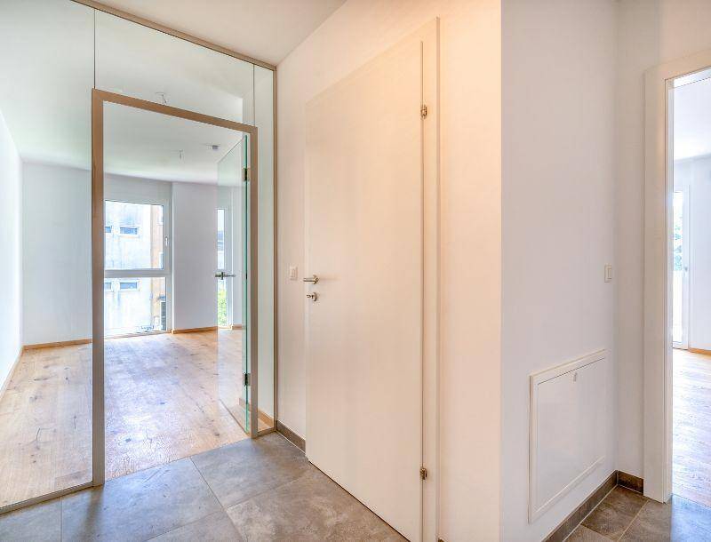 Heller Eingangsbereich mit Fliesenboden und einer modernen Glastür, die zu den Wohnräumen führt.