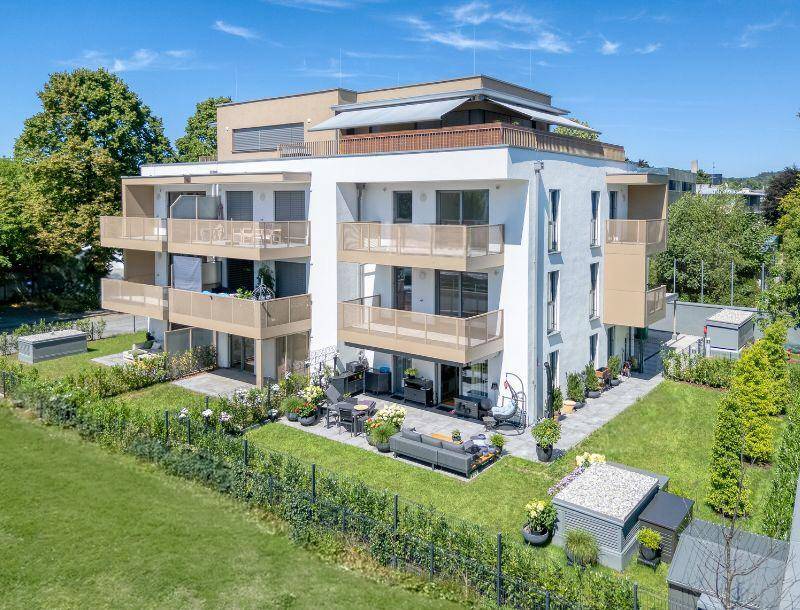 Modernes Mehrfamilienhaus mit mehreren Balkonen, Terrassen und gepflegten Grünflächen.