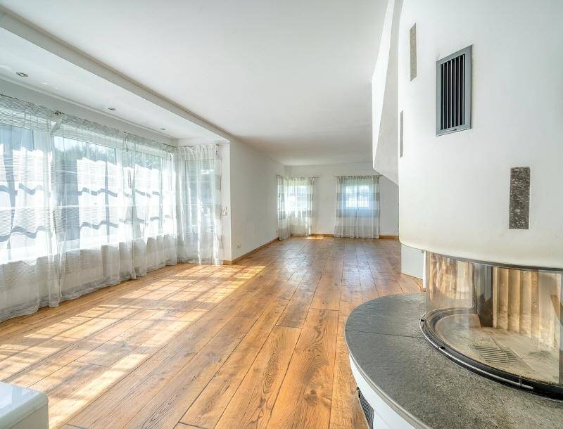 Helles, leeres Wohnzimmer mit breiten Holzdielen und modernem Kaminofen.