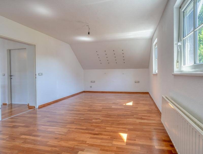Geräumiger Dachbodenraum mit schrägen Wänden, Holzfußboden und Fenster.