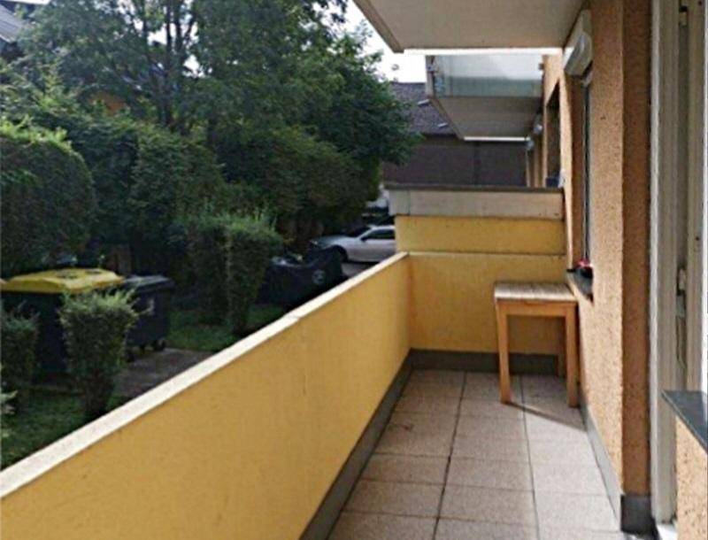 Schmaler Balkon mit gelber Brüstung und Blick ins Grüne sowie auf Mülltonnen.