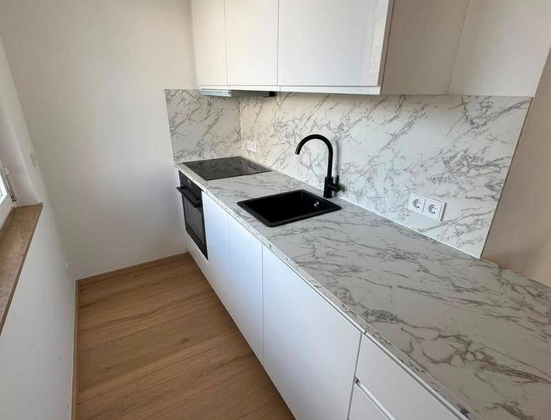 Moderne Küchenzeile mit weißen Schränken, Marmoroptik-Arbeitsplatte und schwarzer Spüle.
