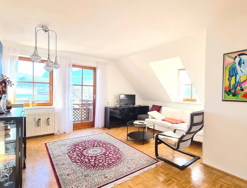 Helles Wohnzimmer mit Dachschräge, Parkettboden und Zugang zu einem Balkon.