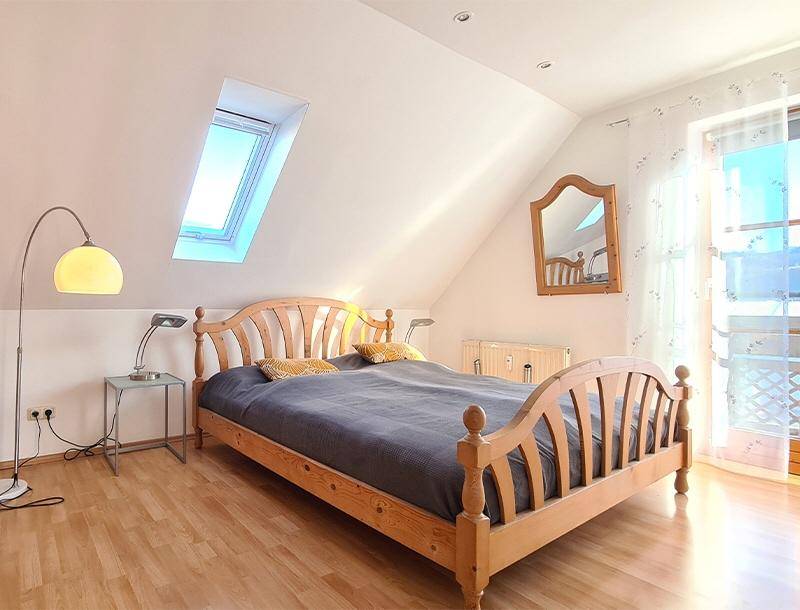 Gemütliches Schlafzimmer mit Holzbett, Parkettboden, Dachfenster und Balkonzugang.