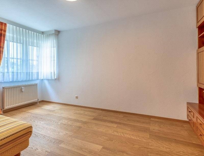 Helles Zimmer mit Holzboden, großem Fenster und Heizkörper, bereit zur individuellen Gestaltung.