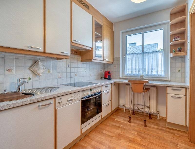 Funktionale Küche mit hellen Holzschränken, Einbaugeräten und einem kleinen Essbereich am Fenster.