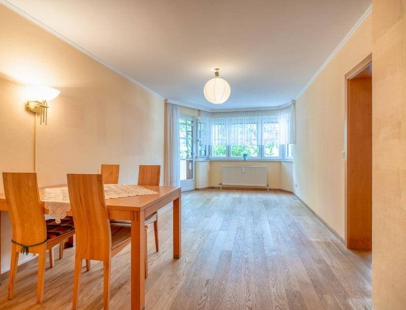 Heller Wohn-Essbereich mit Holzboden, Esstisch und großen Fenstern mit Vorhängen.