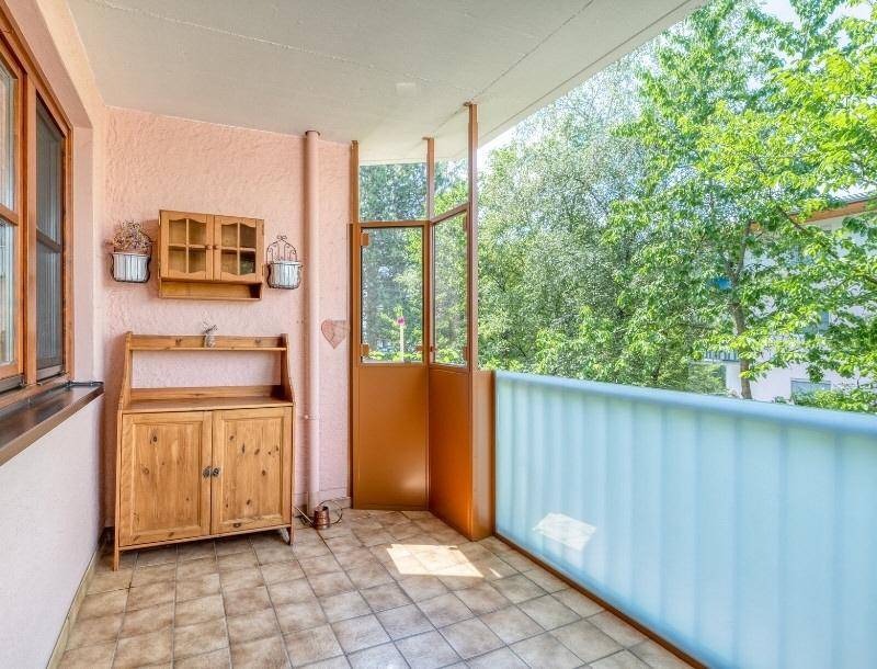 Gemütlicher Balkon mit Fliesenboden, Holzmöbeln und Blick ins Grüne.