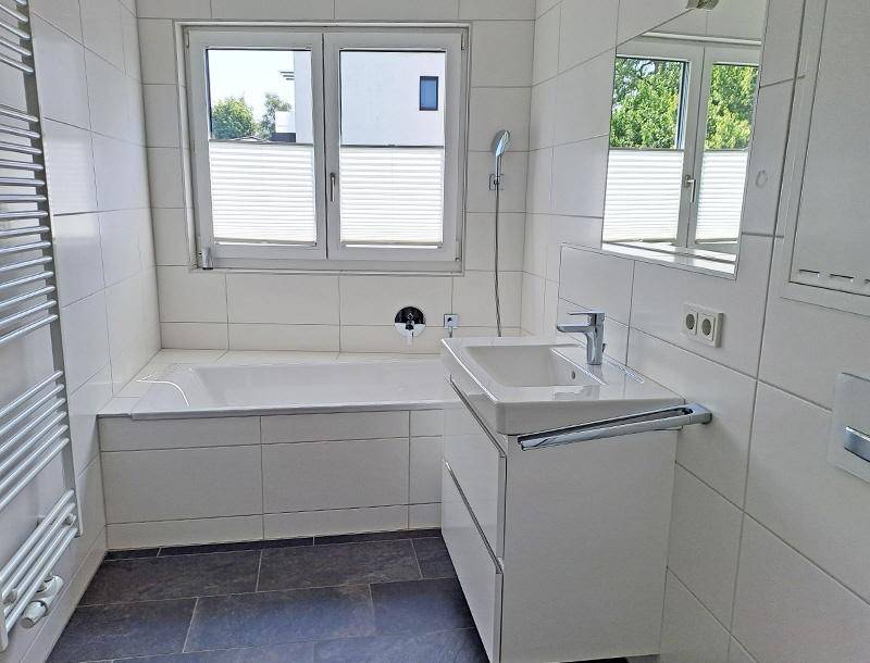Modernes Badezimmer mit Badewanne, Einzelwaschbecken, weißen Fliesen und Fenster.