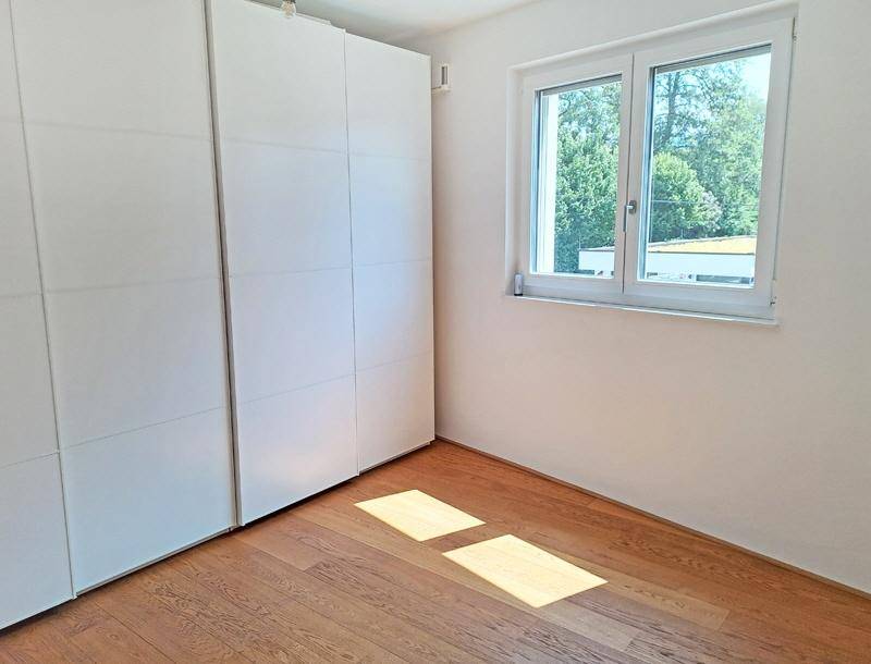 Helles Schlafzimmer mit Einbauschränken, Holzboden und einem Fenster mit Blick ins Grüne.