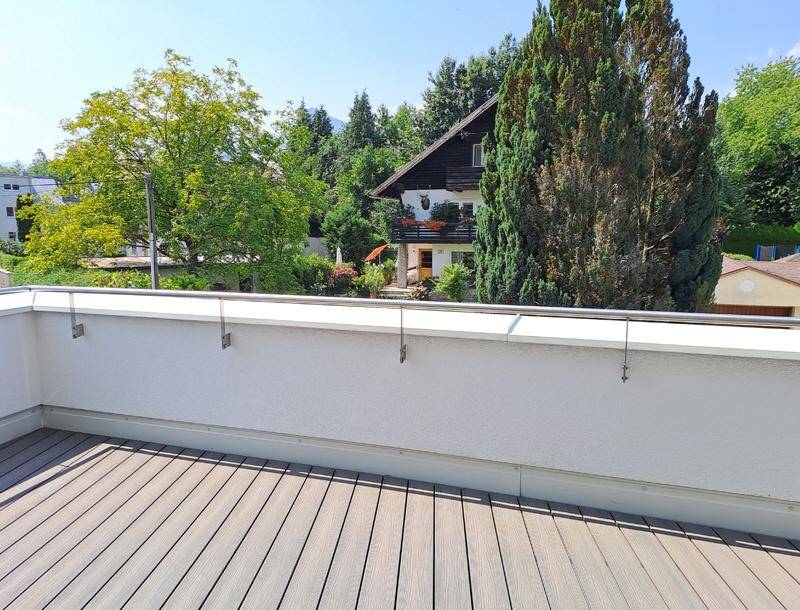 Geräumige Terrasse mit Holzboden und Blick auf ein traditionelles Haus und grüne Bäume.