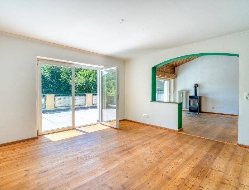Heller Wohnbereich mit Holzboden, Kaminofen und großen Glastüren, die zur sonnigen Terrasse führen.